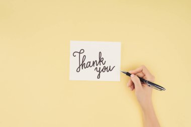 cropped person holding pen and white postcard with thank you lettering isolated on yellow background clipart