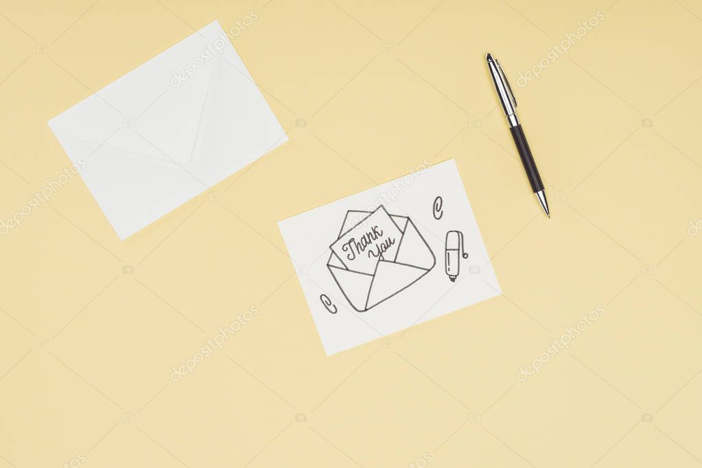 white card with thank you lettering sticking out of hand drawn envelope and pen isolated on yellow background