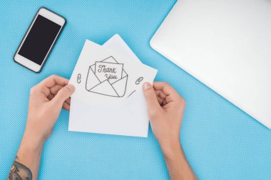 Teşekkürler zarf ve smartphone üzerinde mavi arka plan izole dışına taşıyorsa yazı kağıt tutan kırpılmış kişi