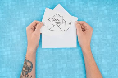 cropped person holding paper with thank you lettering sticking out of envelope isolated on blue background clipart