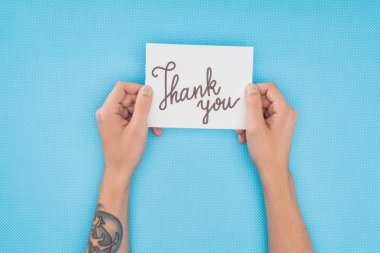 cropped person holding paper with thank you lettering isolated on blue background clipart