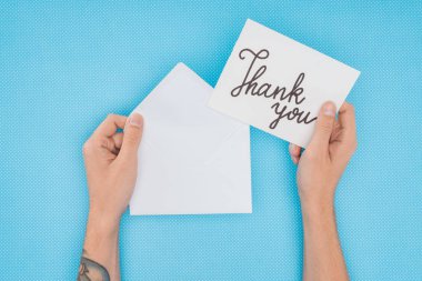cropped person holding paper with thank you lettering isolated on blue background clipart