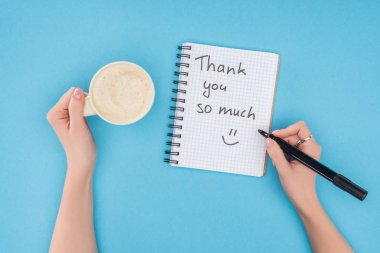 cropped person holding pen and cup of coffee above notebook with thank you so much lettering isolated on blue background clipart