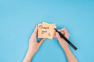 cropped person holding pen above colorful sticky notes with thank you lettering isolated on blue background clipart