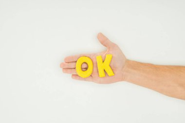 cropped view of person holding ok word in yellow cookies isolated on white background clipart