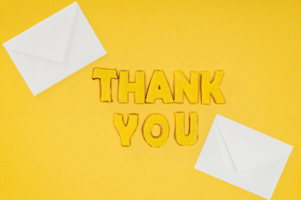 thank you lettering in cookies with white envelopes isolated on yellow background