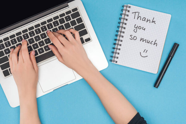 cropped view of woman working on computer and notebook with thank you so much lettering isolated on blue background