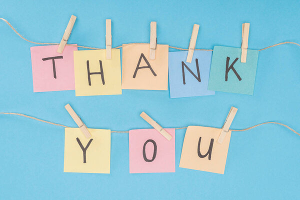 colorful sticky notes spelling thank you on lace with clothespins isolated on blue background