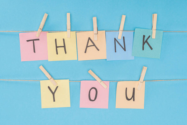 colorful sticky notes spelling thank you on lace with clothespins isolated on blue background