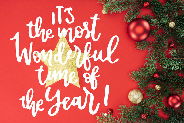 flat lay with pine tree branches with red and golden christmas balls and golden star isolated on red with "its the most wonderful time of year" inspiration