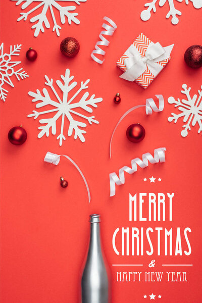top view of present, champagne bottle, red christmas toys, white ribbons and decorative snowflakes arranged isolated on red with "merry christmas and happy new year" lettering