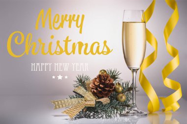 glass of champagne, christmas decoration and confetti on grey backdrop with 