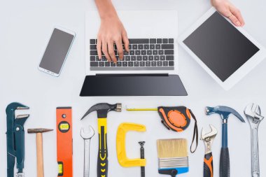 cropped shot of woman using gadgets with various tools lying on white