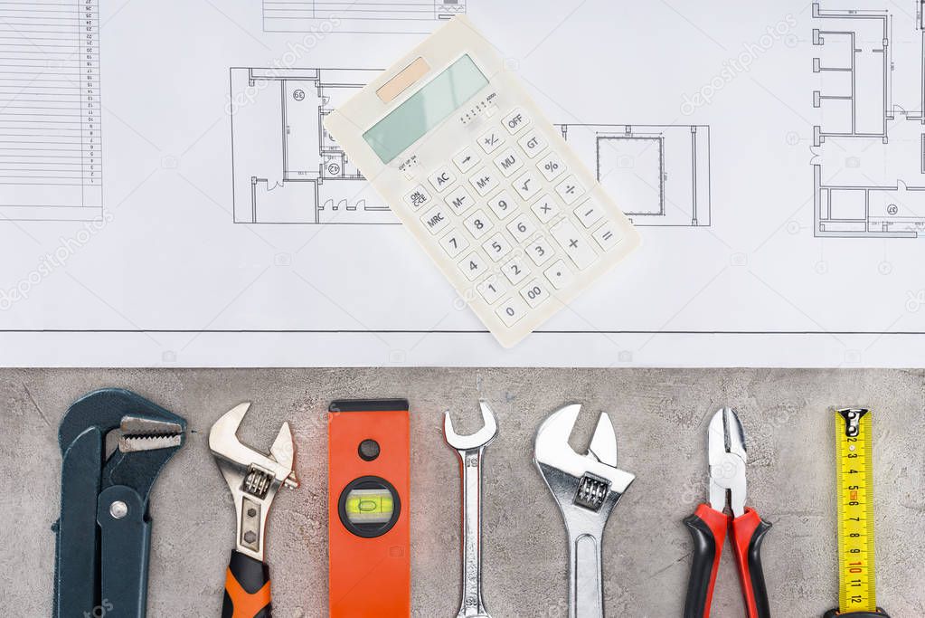 top view of building plan with row of various tools and calculator on concrete surface