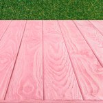 Surface of pink wooden planks on green grass background