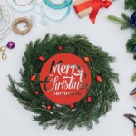 Vista superior de decorações de grinalda de natal artesanal, tesouras e fitas isoladas em branco com letras "Feliz Natal a todos"
