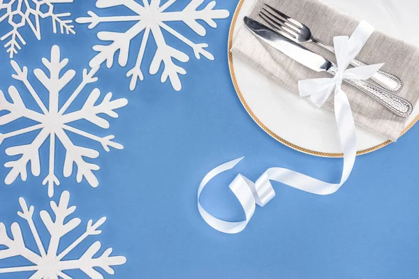 フォークとナイフの青に分離された雪に囲まれたプレートにお祝いリボンでラップの上から見る  — 無料ストックフォト