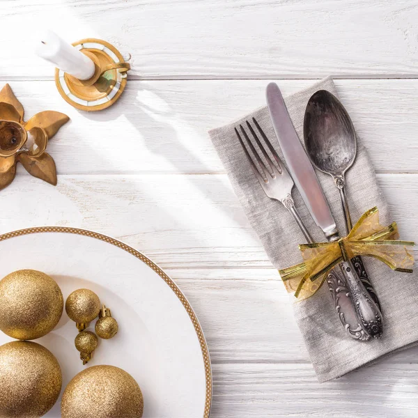 Elevated view of plate with golden christmas balls, candle and fork, spoon, knife wrapped by ribbon on wooden table — Stock Image Elevated View Plate Golden Christmas Balls Candle Fork Spoon Knife Royalty Free Stock Images