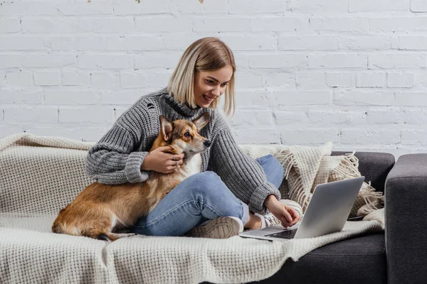 Uśmiechnięta Młoda Blondynka Kobieta Siedzi Welsh Corgi Psa Kanapie Komputera — Zdjęcie stockowe