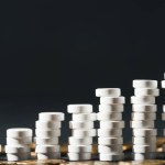 Close up view of arranged stacks made of white pills near pile of coins on grey