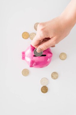 cropped image of woman putting coin into pink piggy bank on white surface clipart