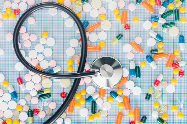 elevated view of various colorful pills and stethoscope on blue checkered surface