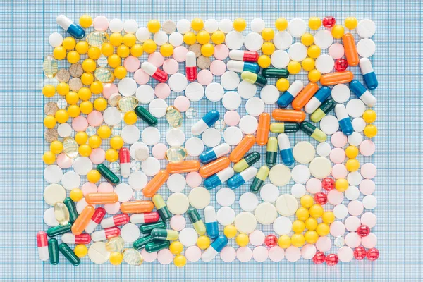 在蓝色格子表面上由各种五颜六色的药丸制成的矩形的顶部视图 — 图库照片