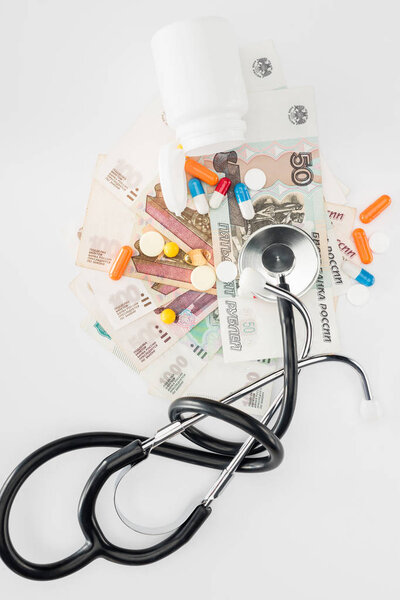elevated view of stethoscope, colorful various pills and russian banknotes on white surface