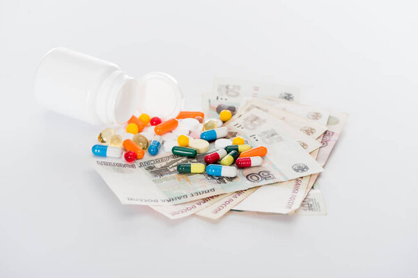 selective focus of pill bottle, russian cash money and various colorful pills on white surface 