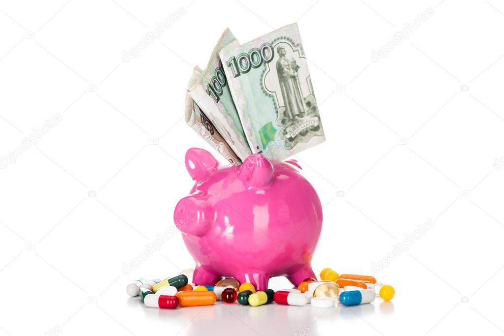 close up shot of pink piggy bank with russian banknote surrounded by various colorful pills isolated on white