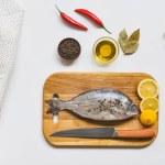 Vista sopraelevata di pesce crudo e vari ingredienti sulla tavola bianca