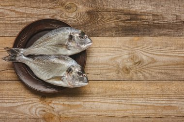 view from above of plate with uncooked fish on wooden table  clipart