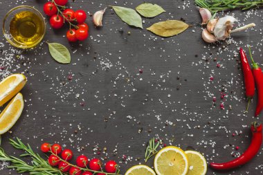top view of cherry tomatoes, garlic, lemon, rosemary, chili and olive oil in glass on black table  clipart