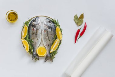 top view of baking paper, olive oil and fish decorated by rosemary and lemon on plate clipart