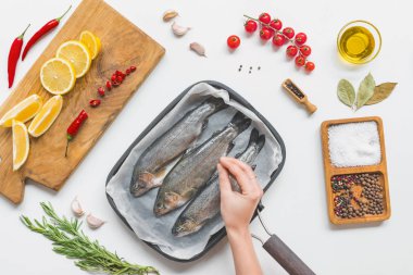 partial view of woman putting salting uncooked fish in baking tray on table with ingredients  clipart