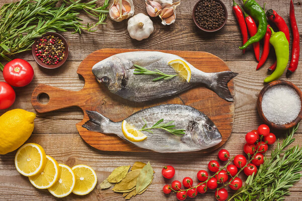 elevated view of raw fish on wooden board surrounded by ingredients on table