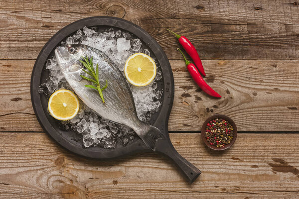 top view of tray with uncooked fish, rosemary and lemon on table