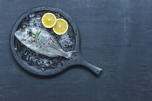 top view of tray with uncooked fish with lemon and rosemary on table