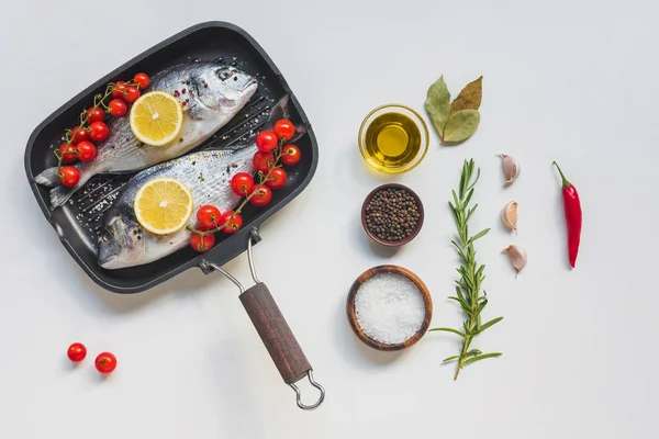 view from above various ingredients, uncooked fish decorated by lemon and cherry tomatoes in baking tray