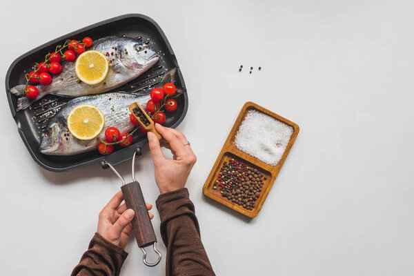 partial view of woman peppering uncooked fish and ingredients in tray