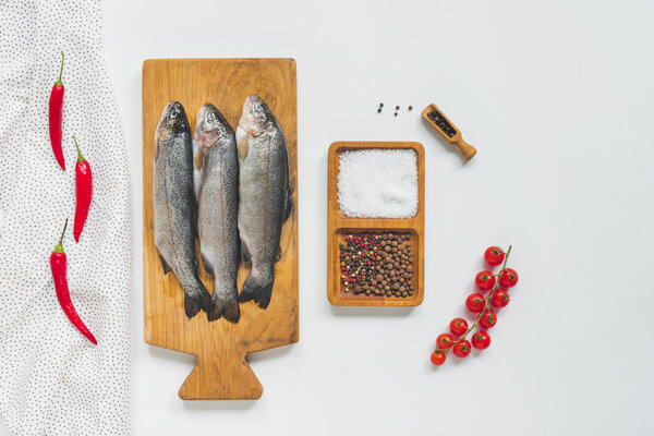 top view of uncooked fish on wooden board near ingredients on white table 