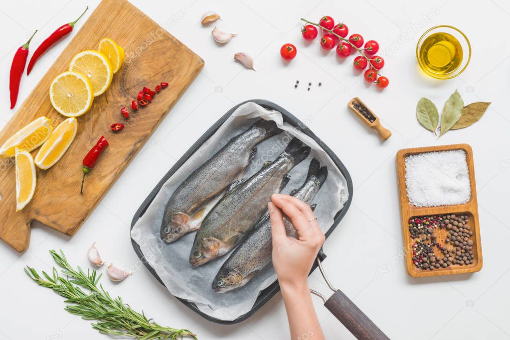 partial view of woman putting salting uncooked fish in baking tray on table with ingredients 