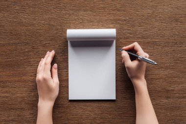 ahşap arka plan üstünde boş defter üzerinde kalem tutan kişinin kırpılmış görünümü