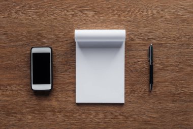 ahşap arka plan üzerinde kalem, defter ile kopya alanı ve smartphone ile boş perde üstten görünüm