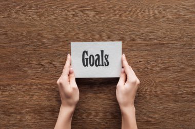 cropped view of woman holding card with 'goals' lettering in hands on wooden background clipart