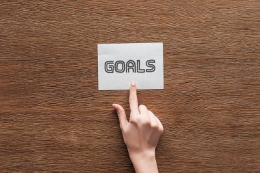 partial view of woman pointing at  'goals' lettering on card with wooden background clipart