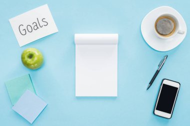 defter üstten görünüm üzerinde mavi arka plan, boş ekran, kahve ve yapışkan notlar ile smartphone