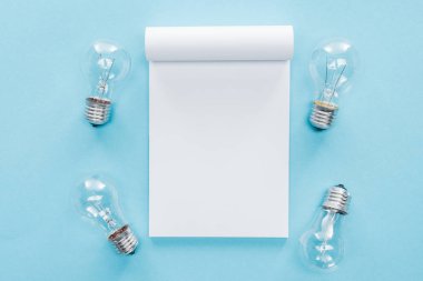 top view of blank notebook with light bulbs on blue background, brainstorming and having idea concept clipart