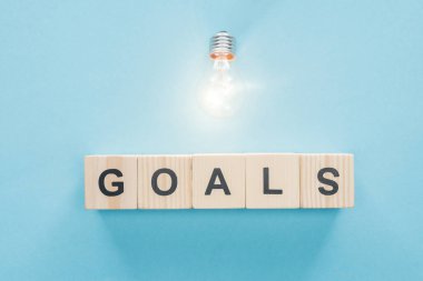 top view of glowing light bulb over 'goals' word made of wooden blocks on blue background, goal setting concept clipart