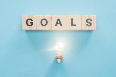 top view of glowing light bulb under 'goals' word made of wooden blocks on blue background, goal setting concept clipart